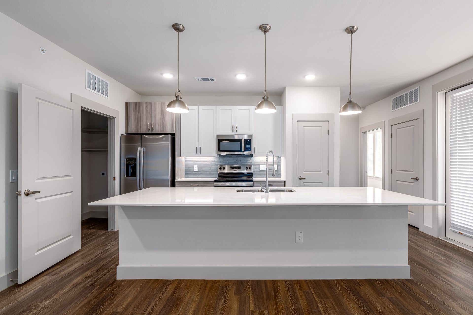 Modern white kitchen with island, stainless steel appliances, pendant lights, and wood flooring