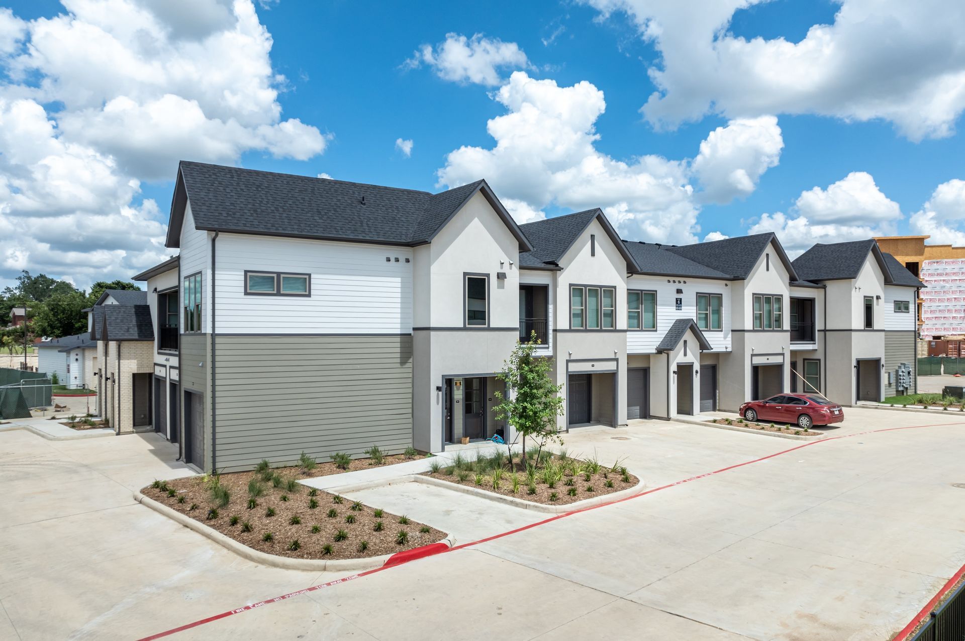 Modern apartment complex with white and gray buildings, parked cars, and a bright blue sky