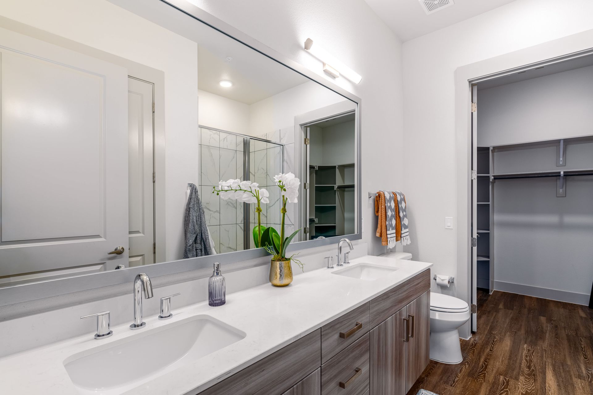 Bright modern bathroom with double vanity, large mirror, and open closet with shelves.