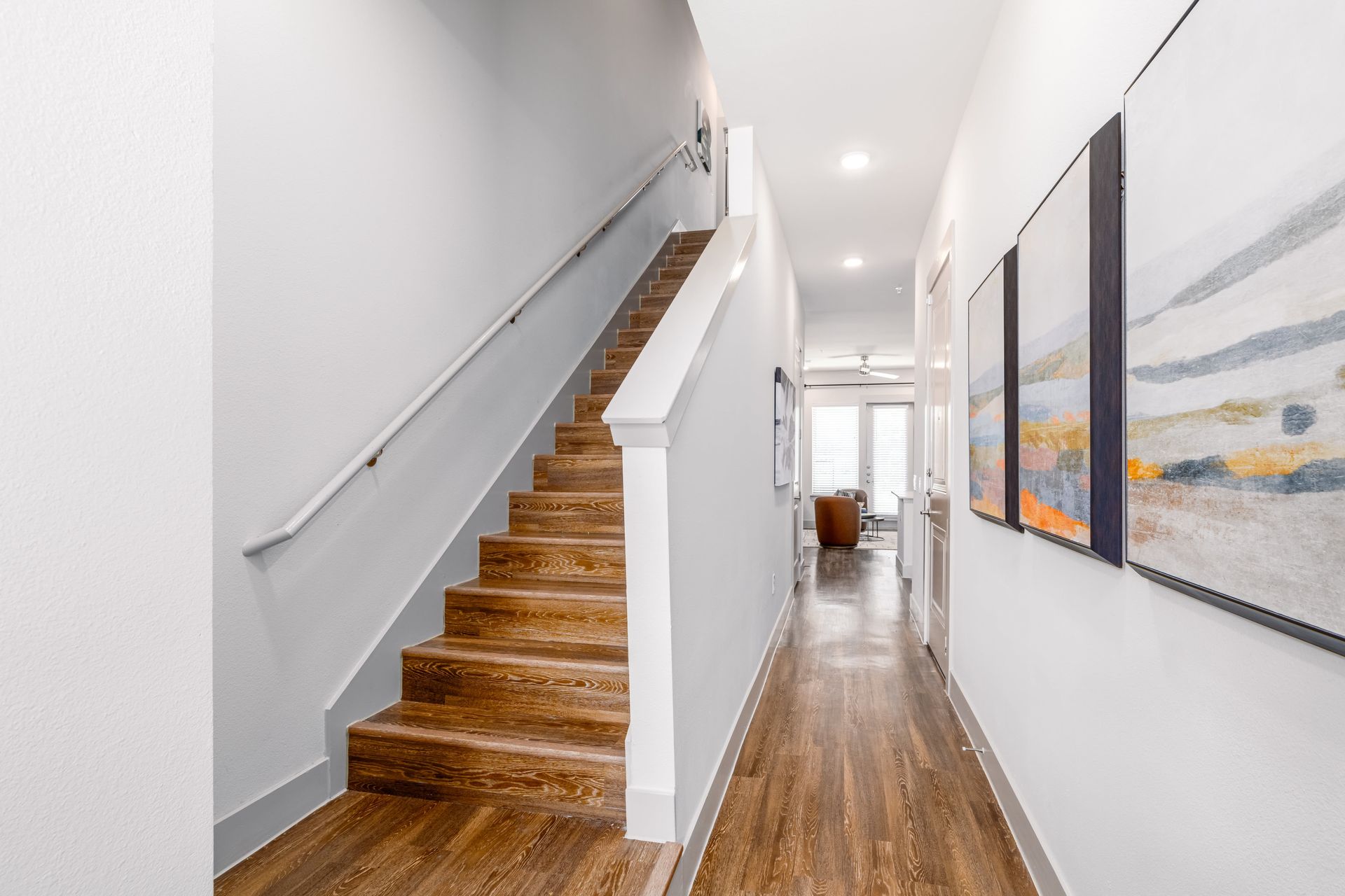 Modern hallway with wooden stairs on the left and framed artwork along a bright white corridor