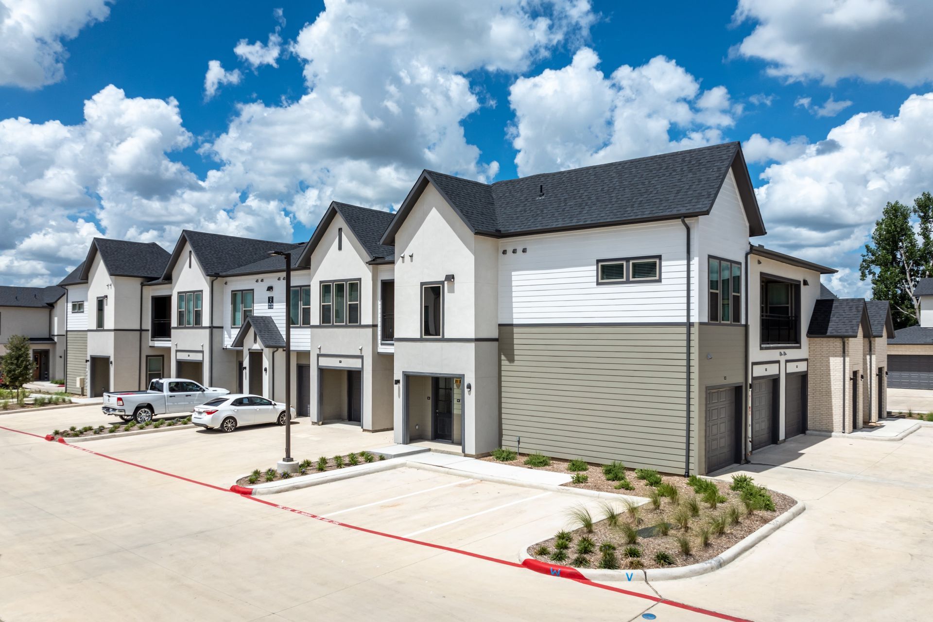 Row of modern suburban townhouses with garages under a bright blue sky and clouds