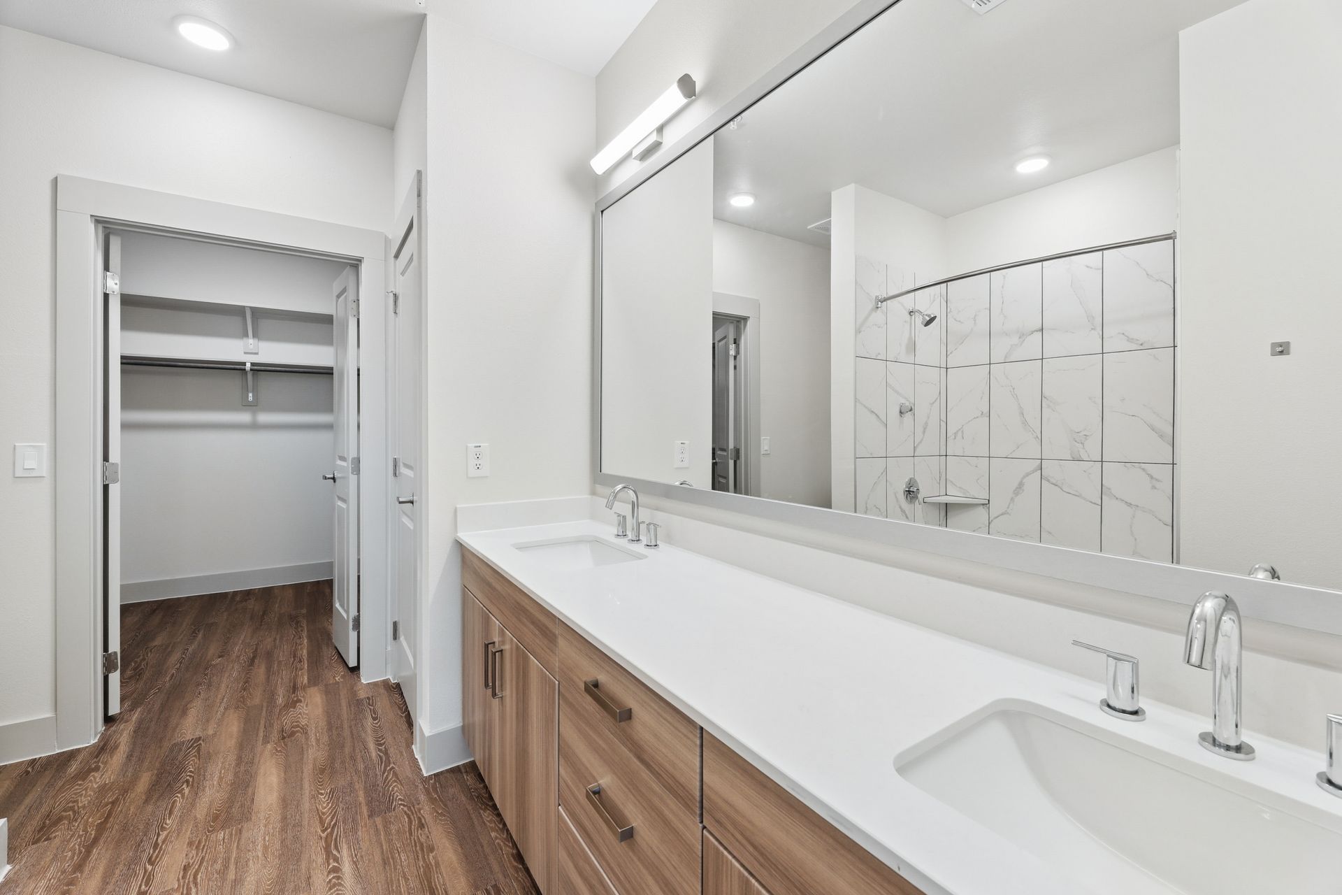 Modern bathroom with double vanity, large mirror, and walk-in closet visible through open doorway