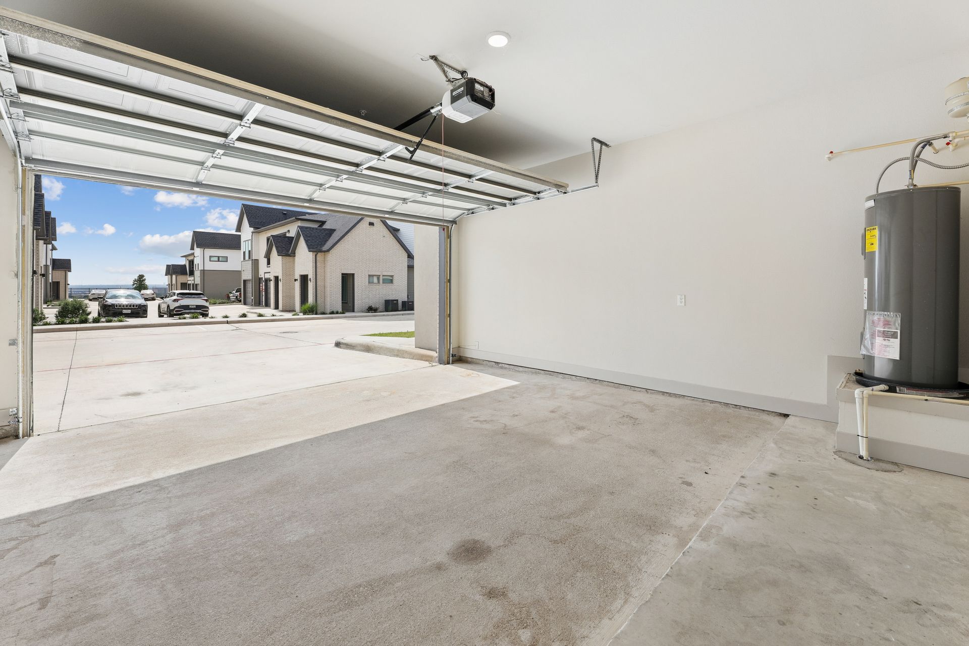 Empty residential garage with open door, concrete floor, and water heater on the right.