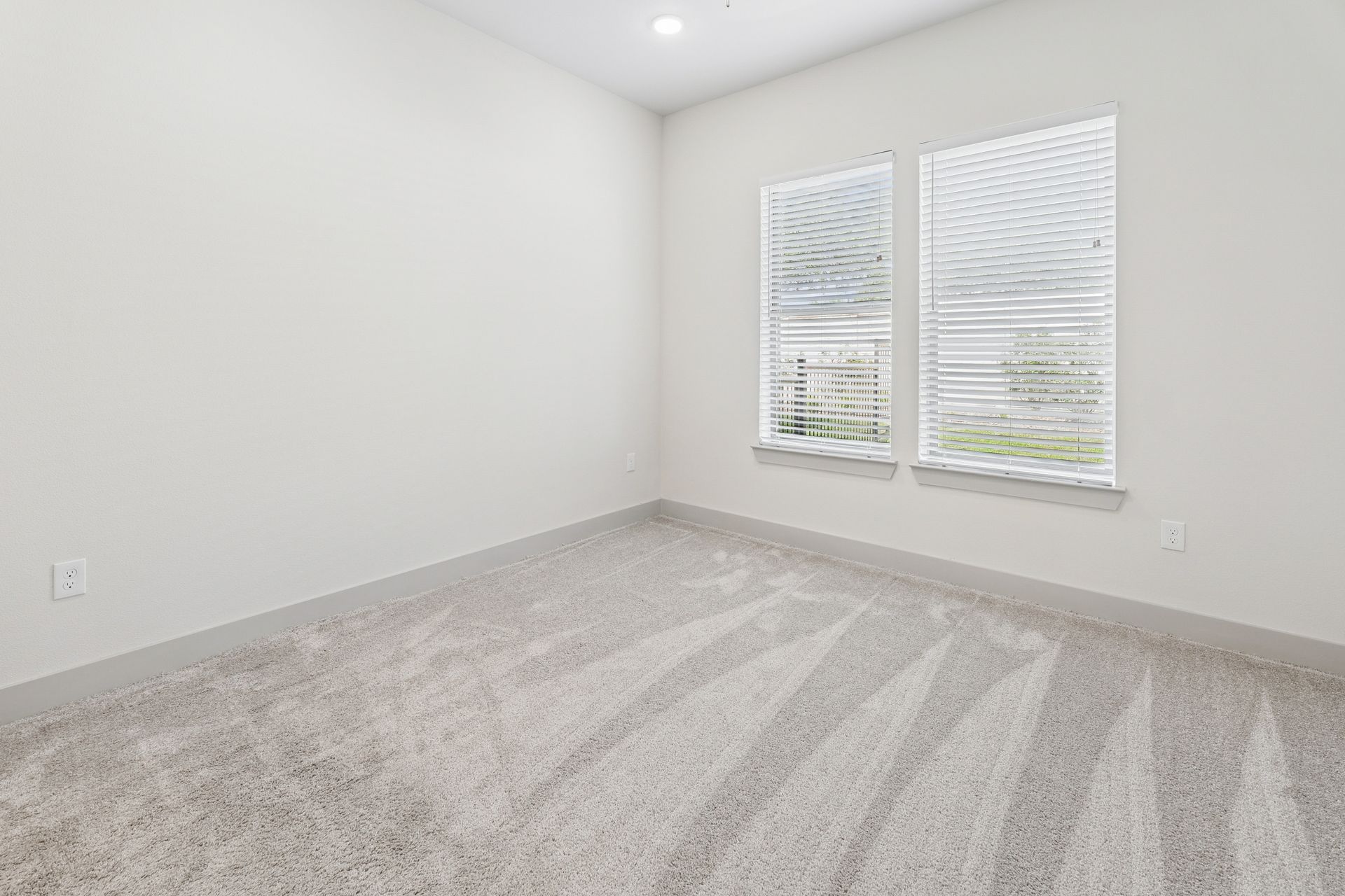 Empty white bedroom with gray carpet and two windows with blinds
