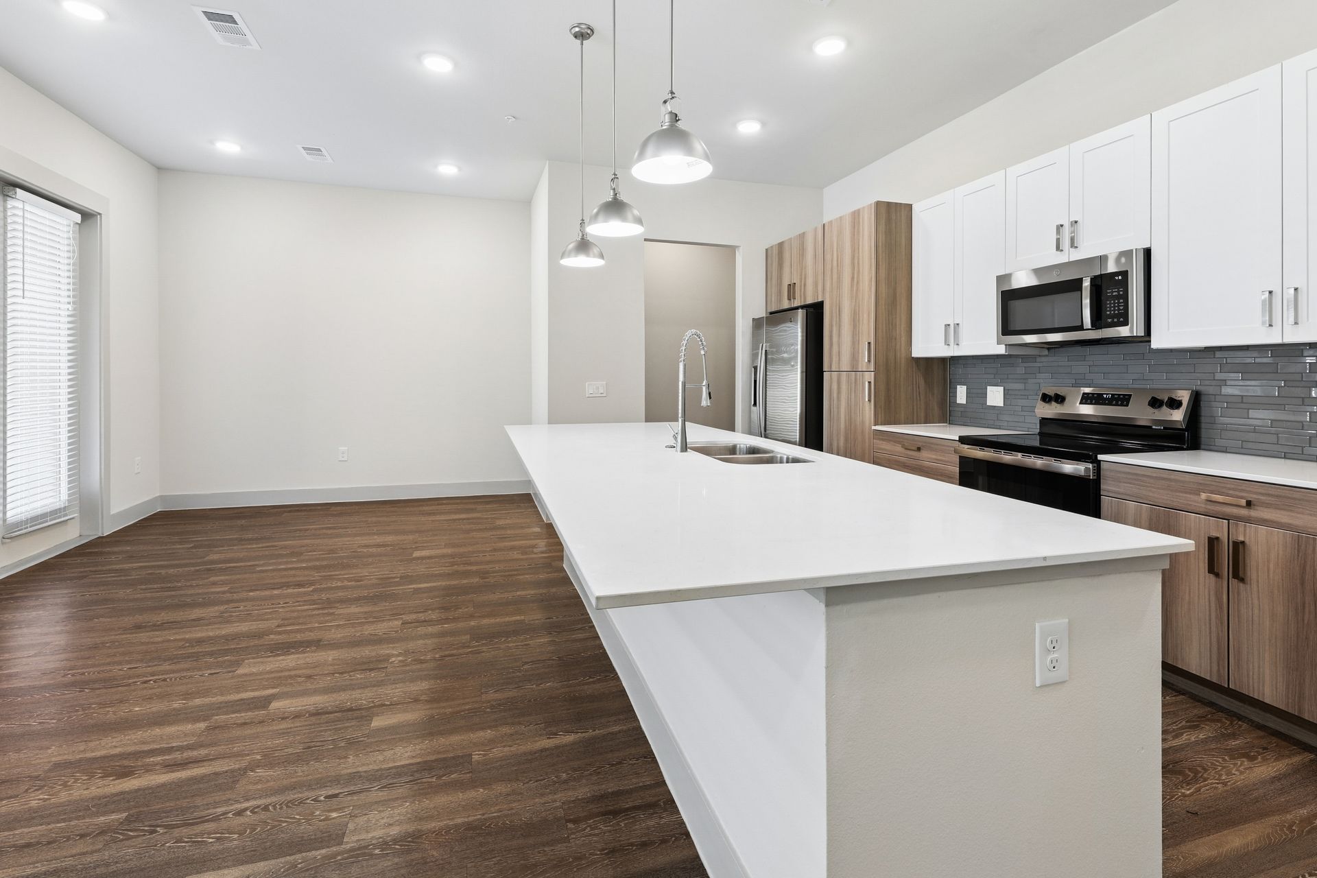 Bright modern kitchen with white island, wood cabinets, stainless appliances, and dark hardwood floors