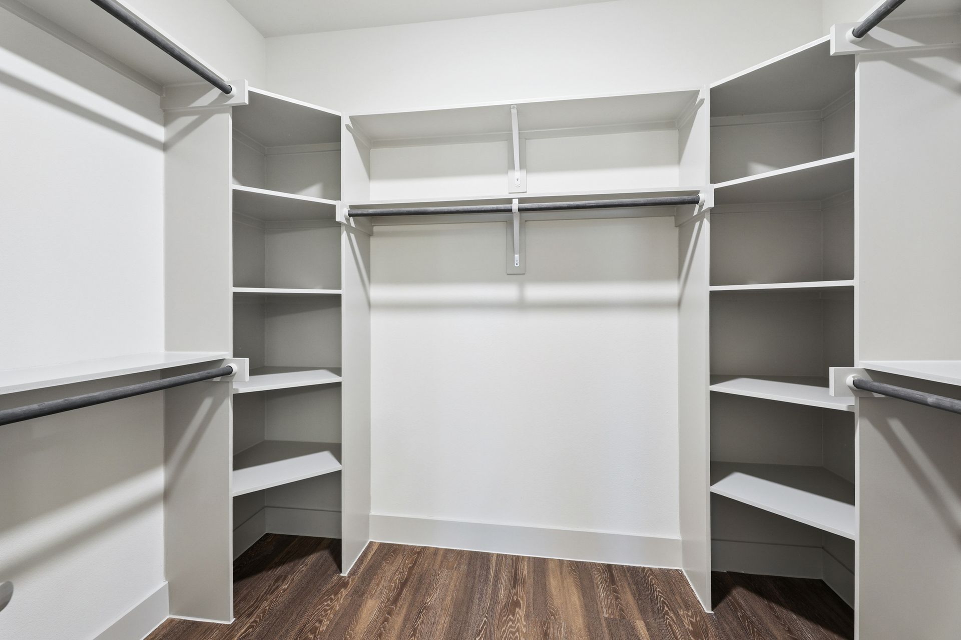 Walk-in closet with white shelves, hanging rods, and wood flooring