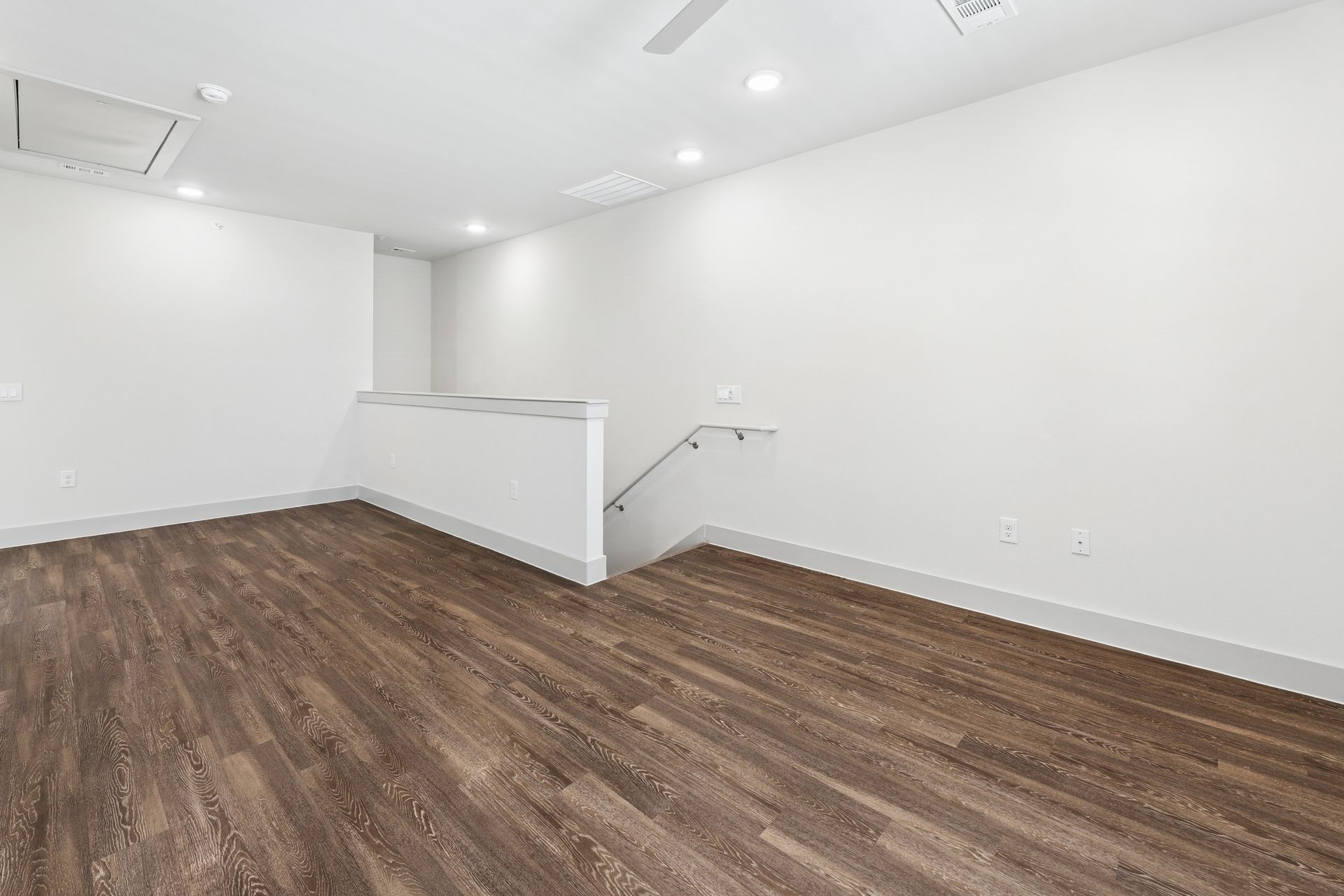 Empty white room with wood flooring and a small stair railing