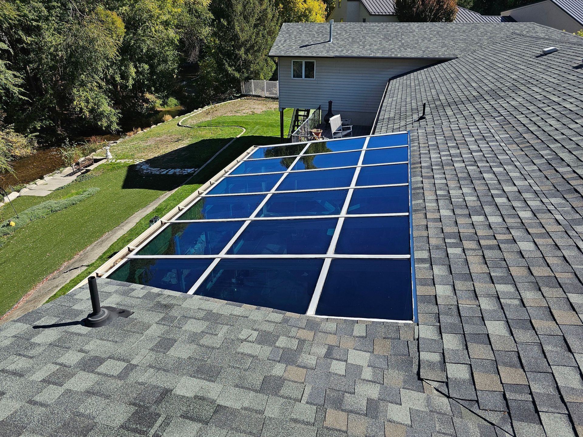 Rooftop pool enclosure with dark blue panels and white framing on a shingled roof, trees in the background.