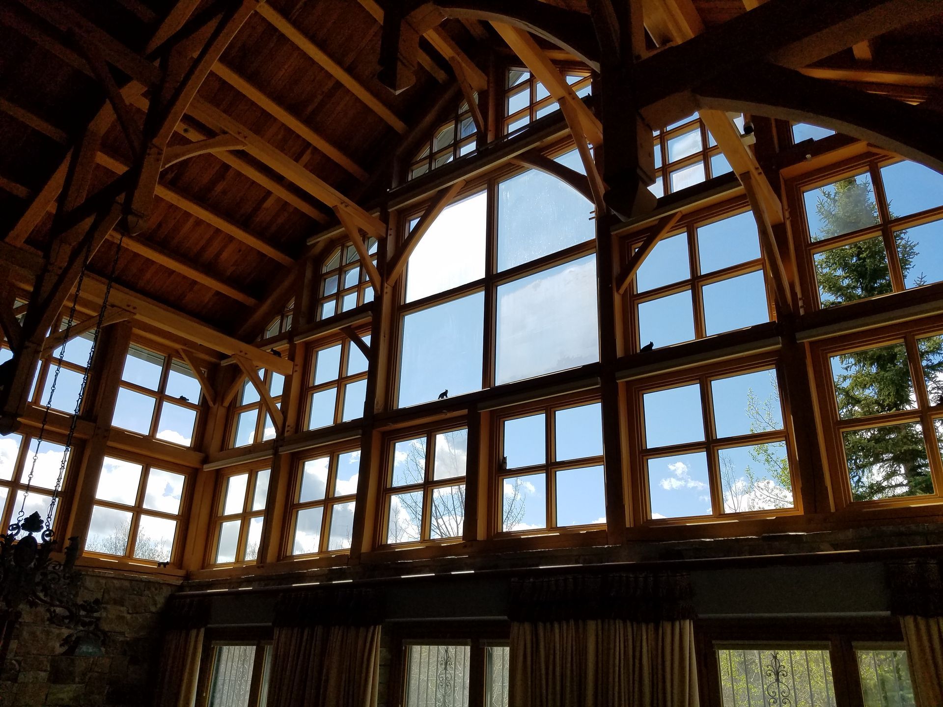 Interior view of a wooden structure with large arched windows showcasing a bright sky.
