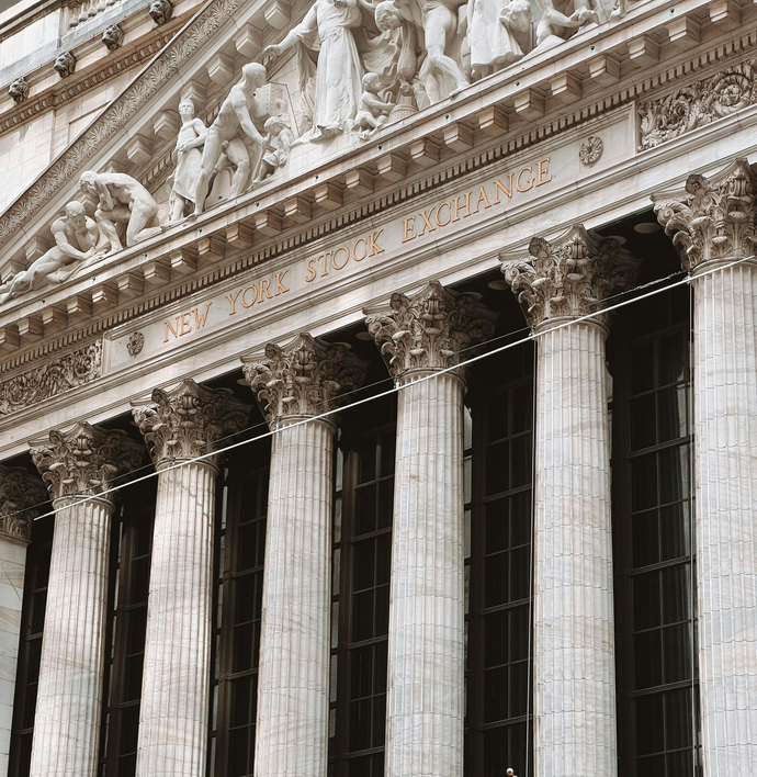 Low-angle view of the New York Stock Exchange building with tall marble columns and neoclassical roof sculptures.