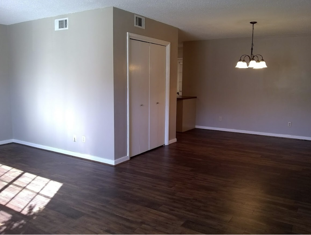 An empty living room with hardwood floors and a chandelier