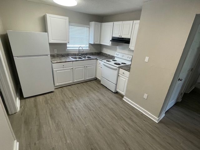 A kitchen with white cabinets , a refrigerator , a stove , and a sink.