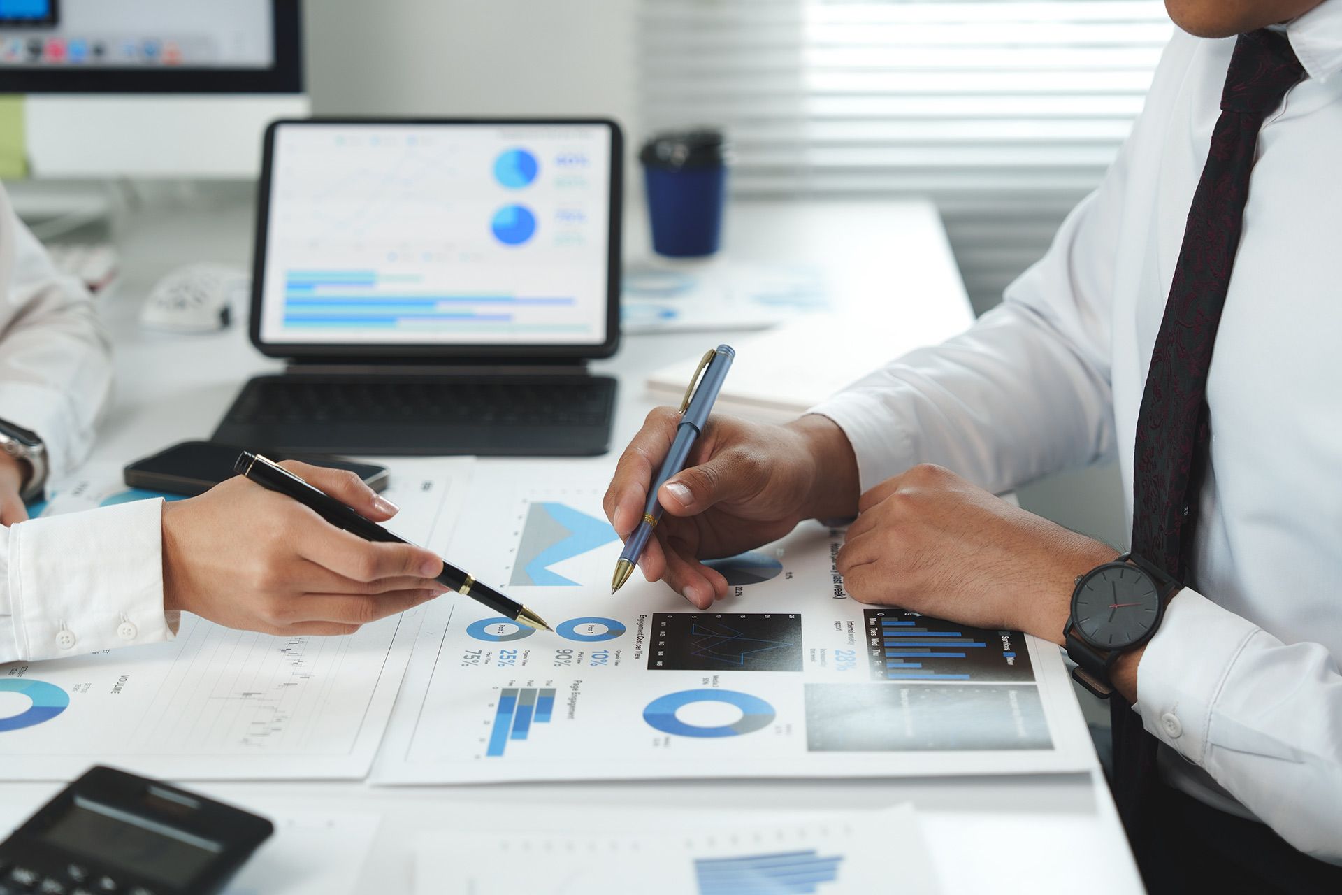 Two people reviewing financial charts on a desk; a tablet and calculator are also visible.