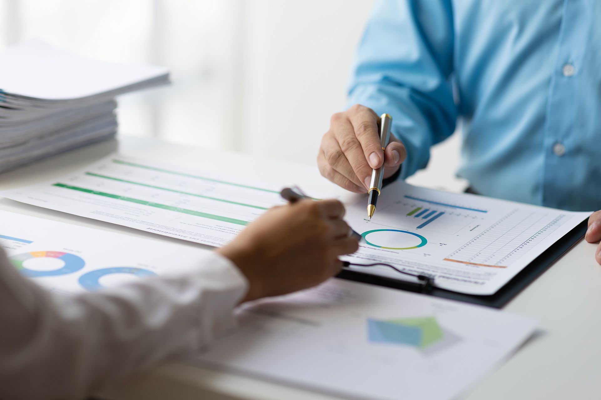 Two people reviewing charts and graphs, one pointing with a pen.