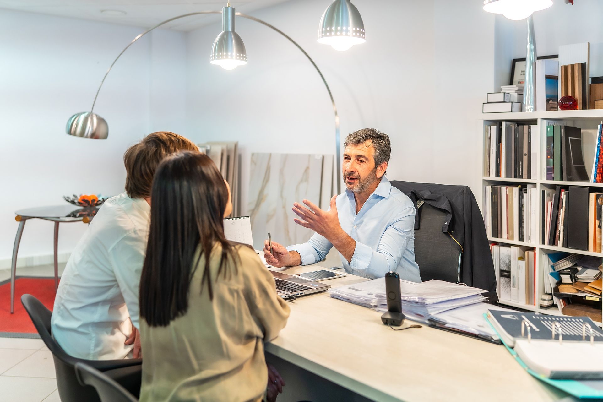 Man advising a couple at a desk, discussing design samples in a showroom.
