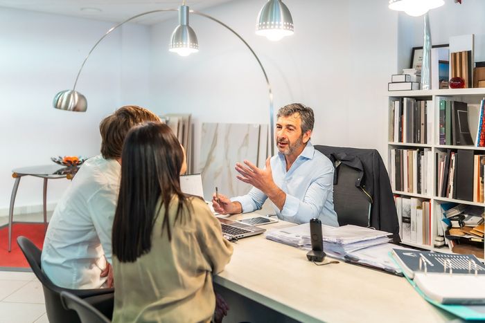 Man advising a couple at a desk, discussing design samples in a showroom.