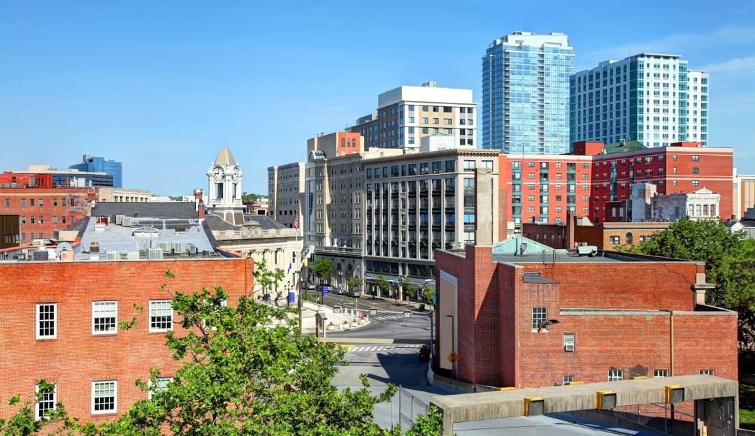 American flag hangs on a pole next to a sidewalk and road in a small town.