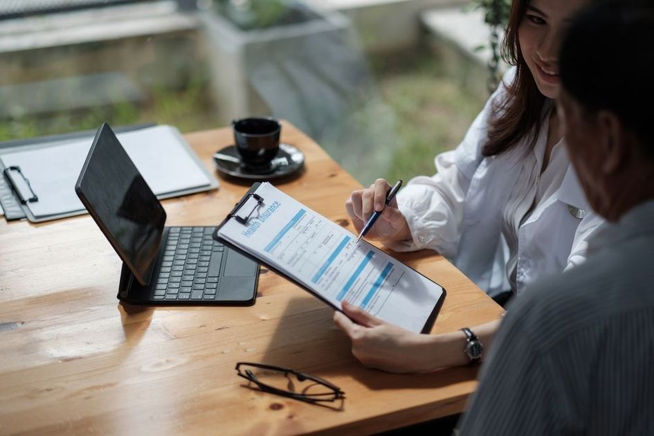 A man and a woman are sitting at a table looking at a clipboard.