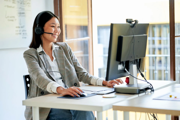 A woman wearing a headset is sitting at a desk in front of a computer.