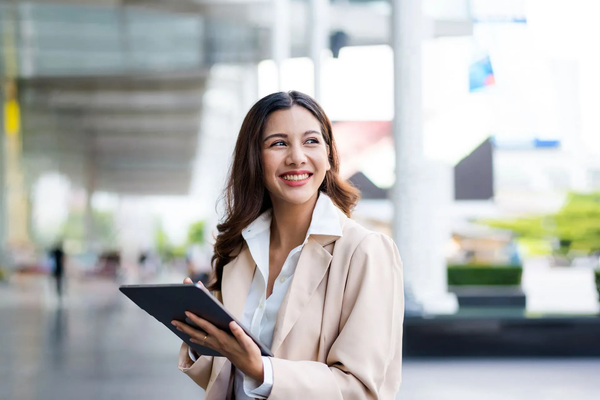 A woman is holding a tablet in her hand and smiling.