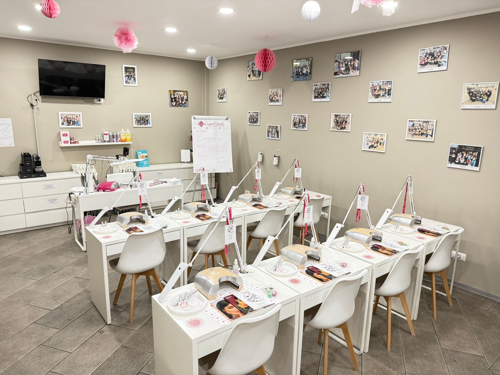 Un salone per unghie con scrivanie, sedie e lampade bianche; foto alle pareti; decorazioni rosa.