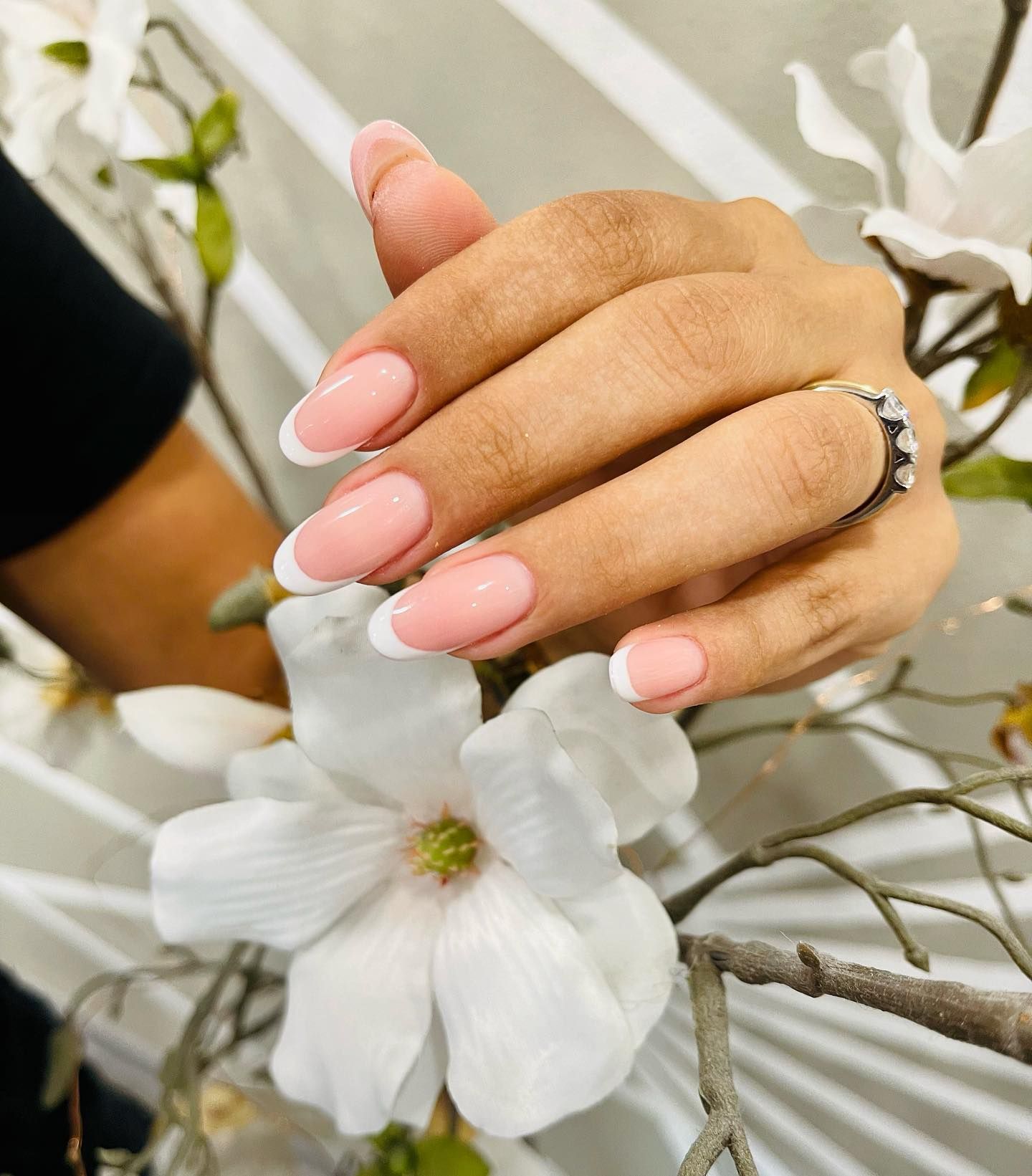 La mano di una donna con le unghie rosa e bianche tiene un fiore bianco.