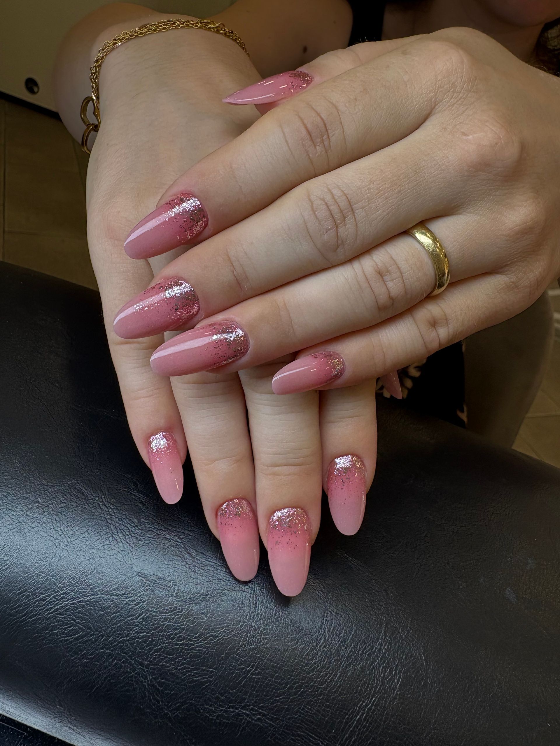 Mani di donna con lunghe unghie rosa sfumate e dettagli glitterati argentati, gioielli dorati.