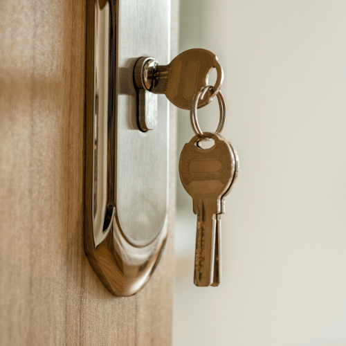 Keys in a door lock on a wooden door, ready to open.