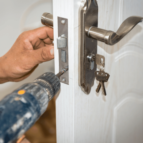 Person using a drill to install a door lock on a white door.
