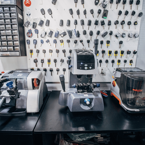 Key-cutting machines on a counter with keys displayed on the wall in a locksmith shop.