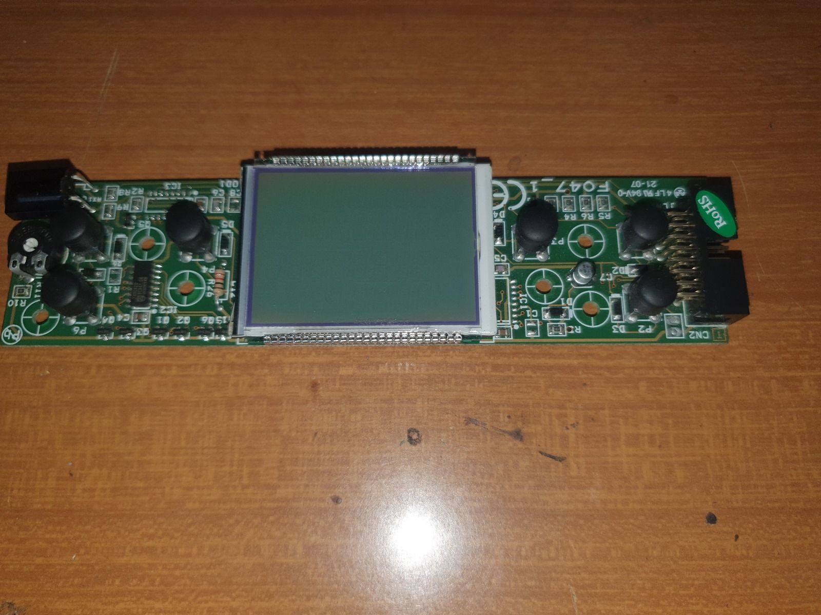 Una scheda madre con uno schermo verde è appoggiata su un tavolo di legno