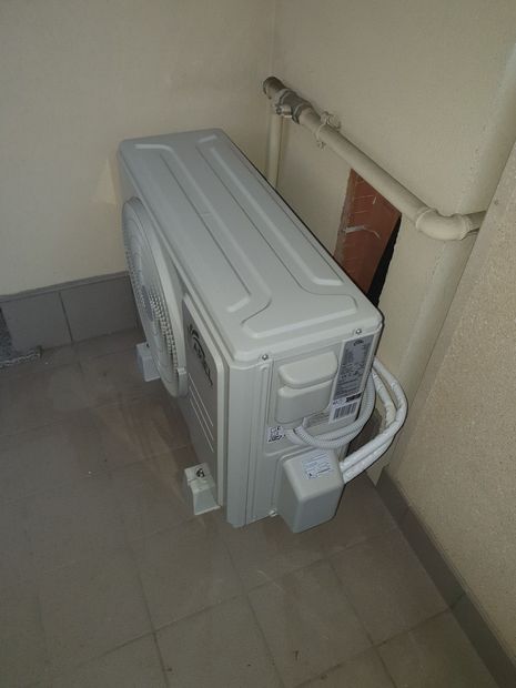 Un condizionatore bianco è appoggiato sul pavimento, accanto a un muro.