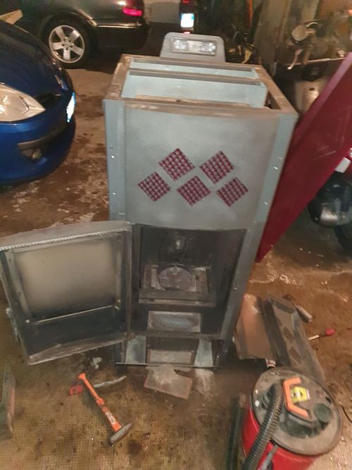 Una stufa con la porta aperta si trova in un garage accanto a un aspirapolvere.