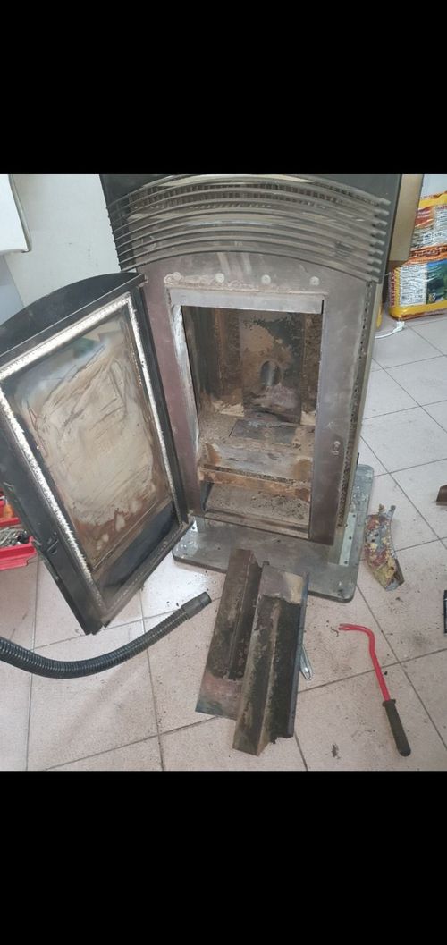 Una stufa a legna con la porta aperta è appoggiata su un pavimento piastrellato.