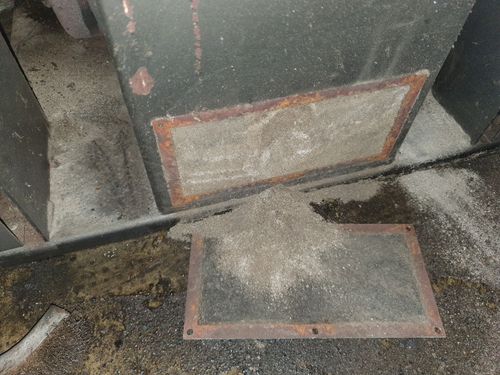 Una porta sporca è appoggiata sul pavimento accanto a un vassoio di metallo.