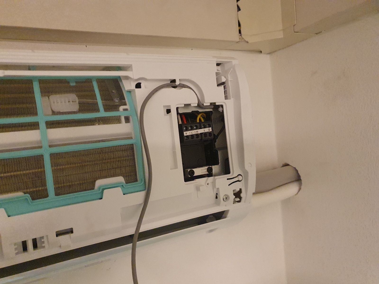 Primo piano di un condizionatore d'aria montato a parete da cui esce un cavo.