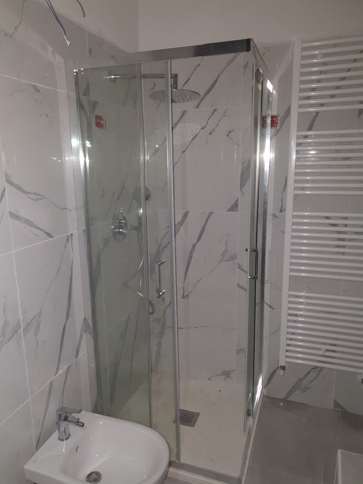 Un bagno con doccia, lavandino e portasciugamani.