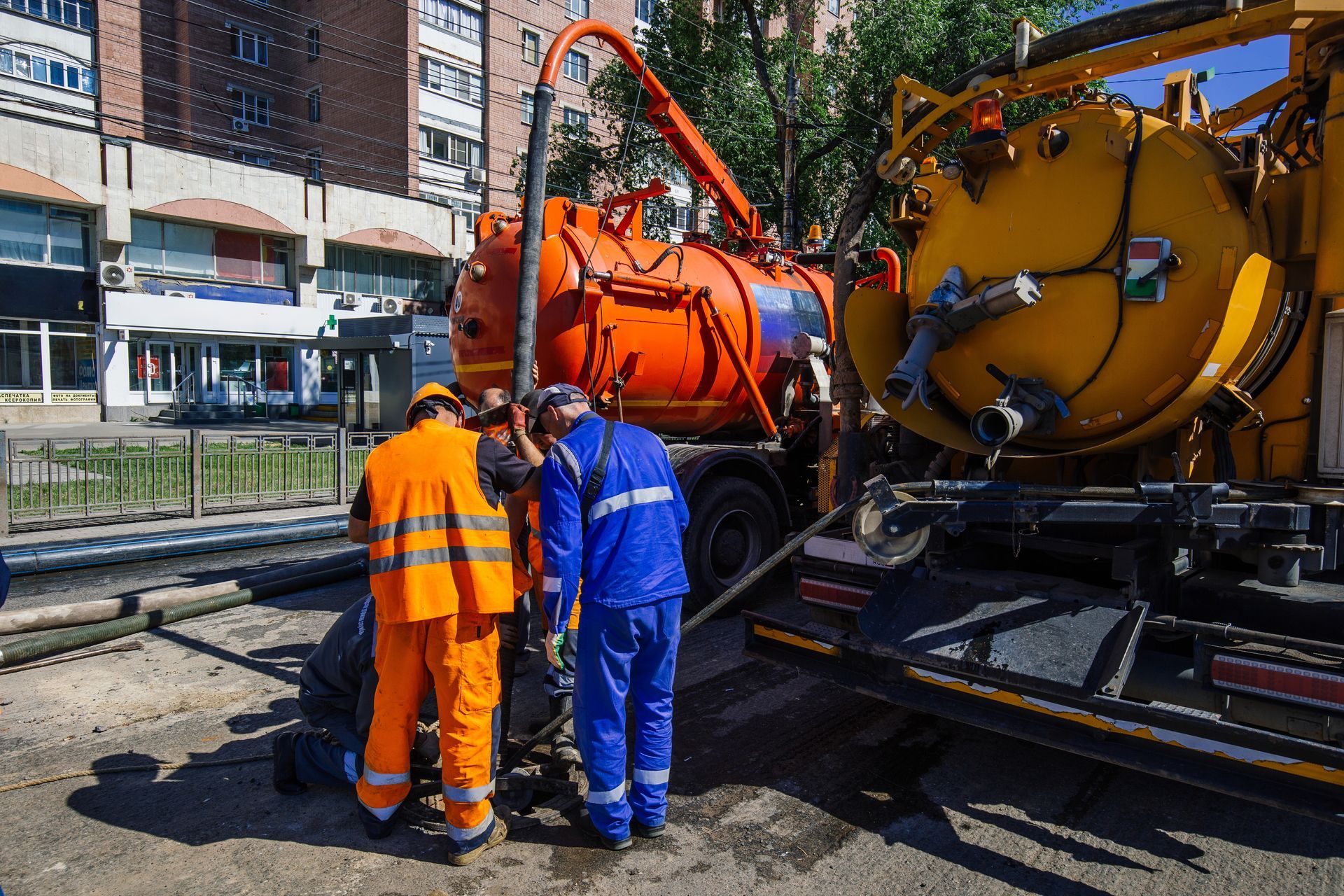 Two workers in high-visibility uniforms operate a vacuum truck during outdoor utility maintenance on a city street.