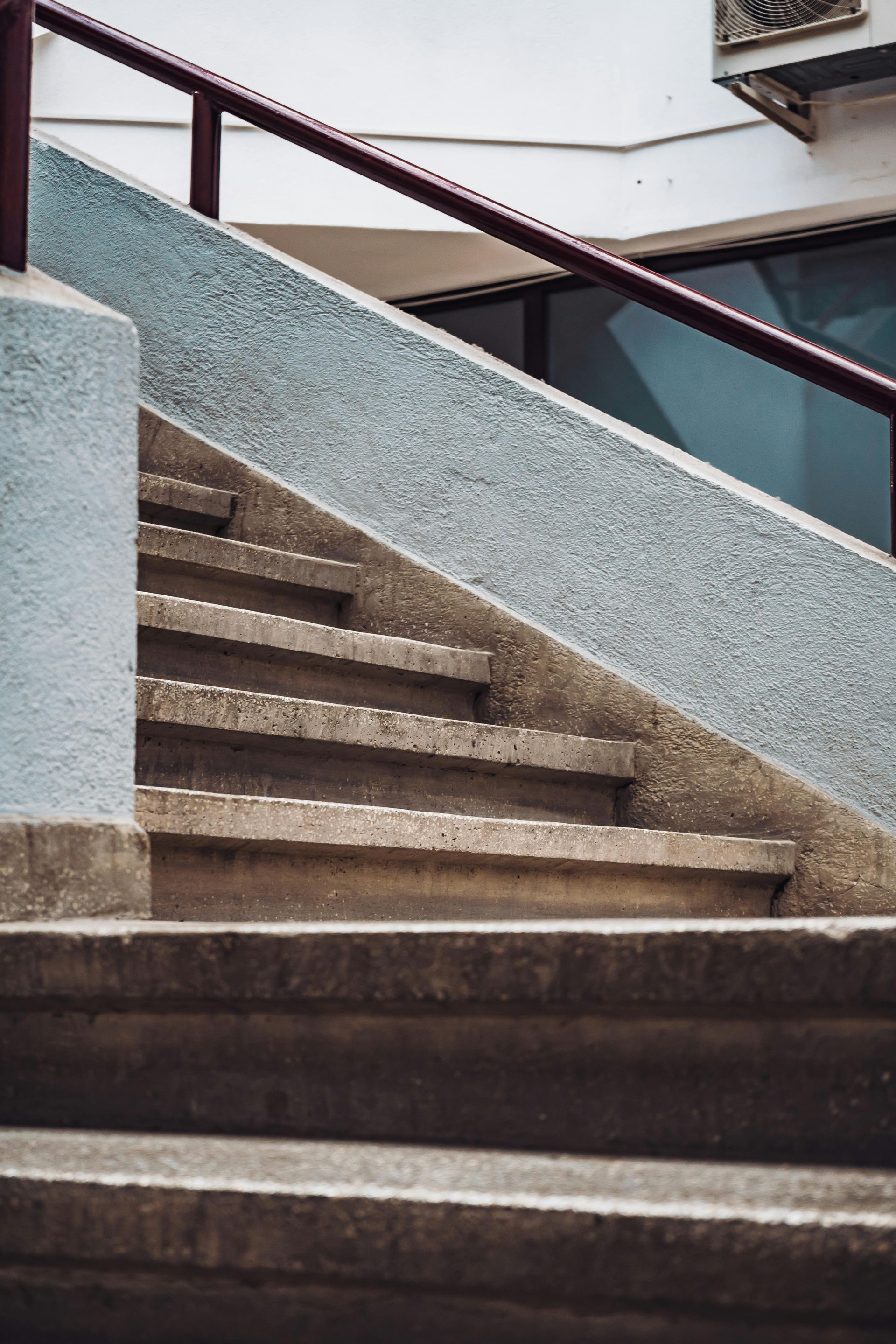 Concrete outdoor stairs with a red handrail, leading upwards.