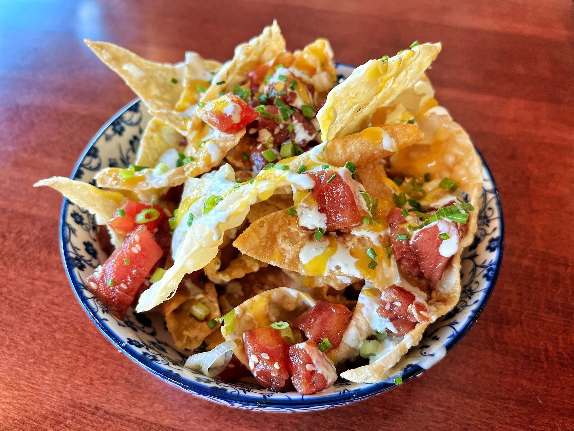A bowl of nachos with tomatoes and cheese on a wooden table.