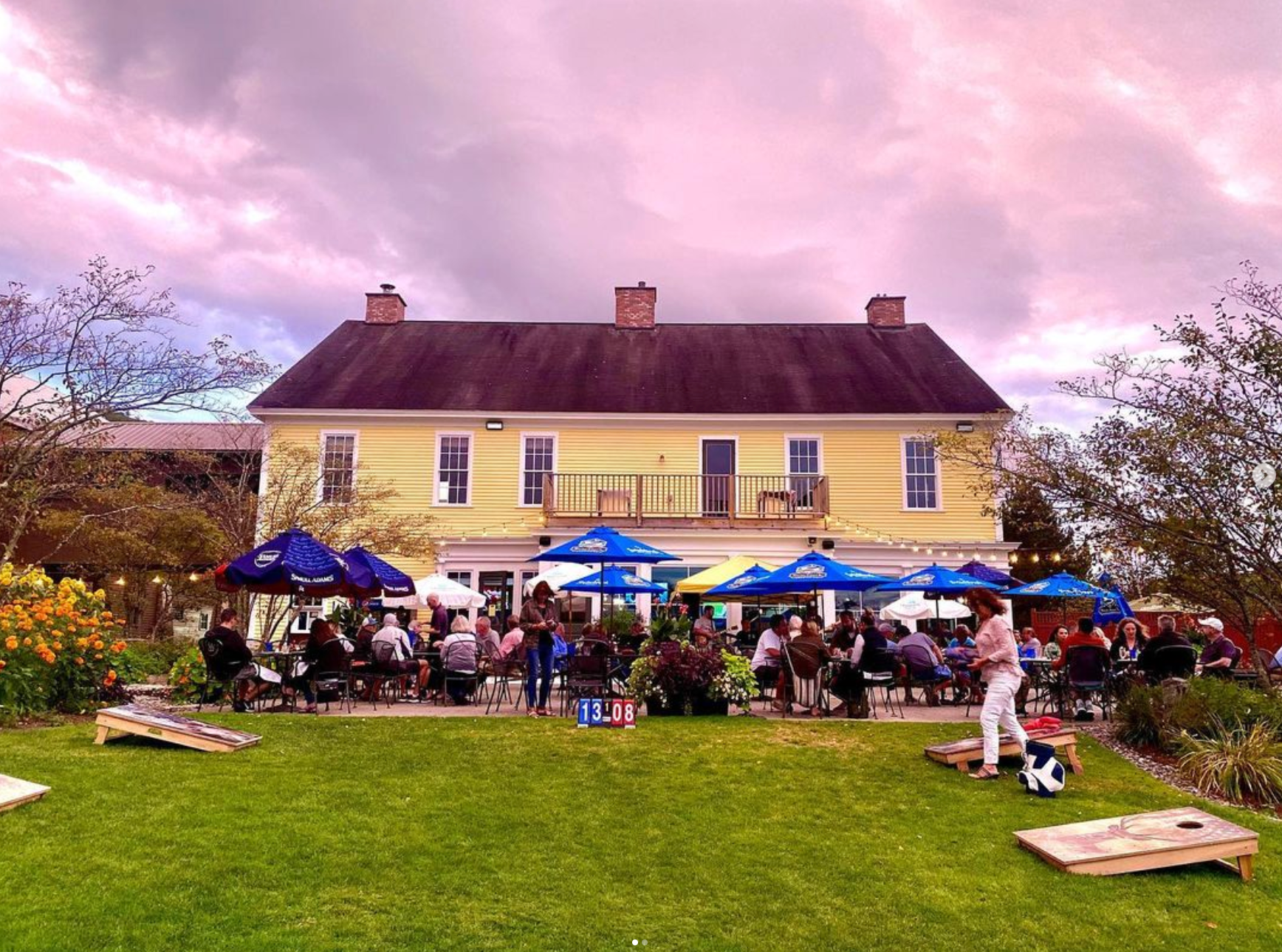 A group of people are playing cornhole in front of a large yellow house.