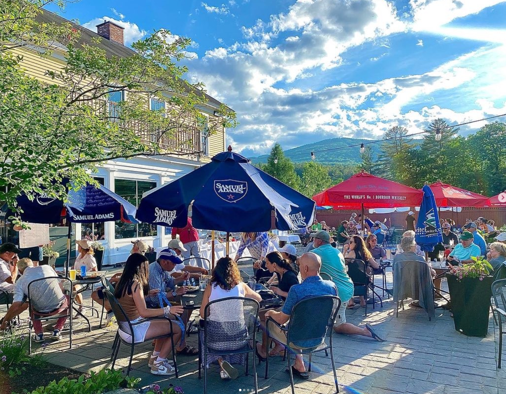 A group of people are sitting at tables under umbrellas outside of a restaurant.