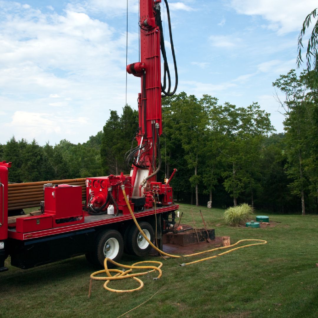 A red truck is parked in a grassy field with trees in the background.
