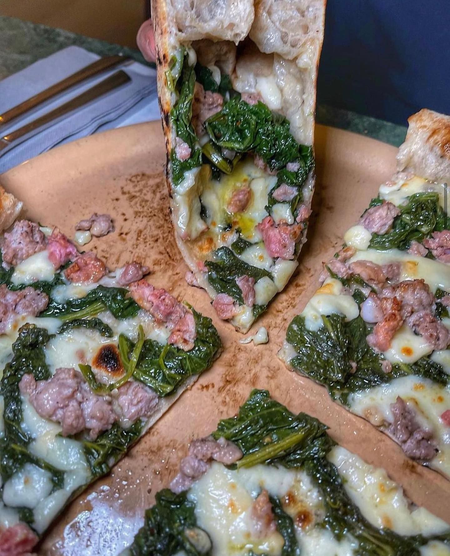 Una pizza con spinaci e salsiccia viene mangiata su un piatto.