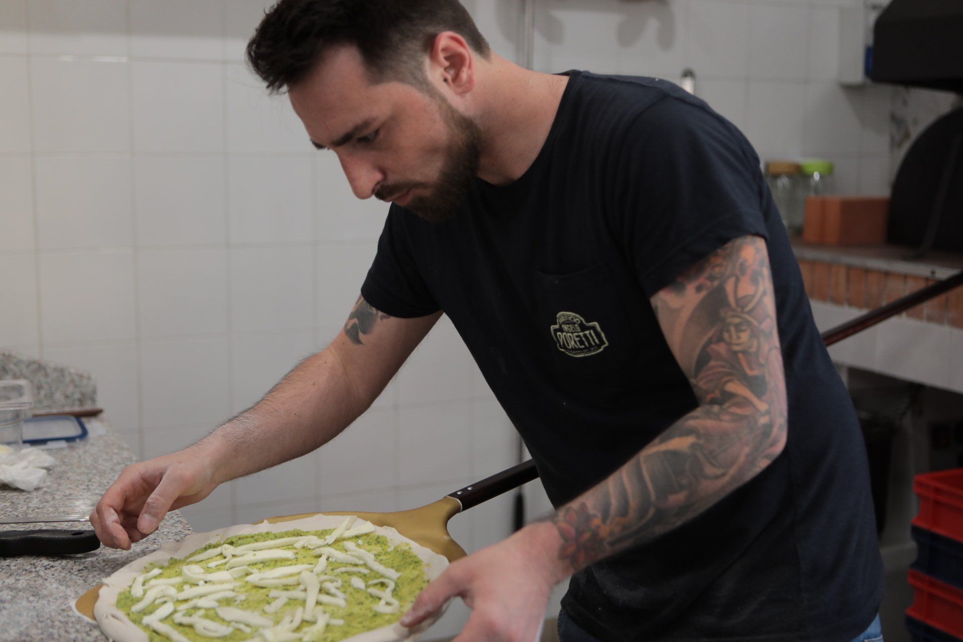 Un uomo con un tatuaggio sul braccio sta preparando una pizza