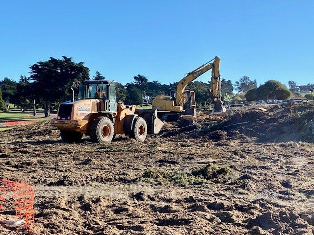 A Case wheel loader and excavator working on muddy ground under a clear blue sky.