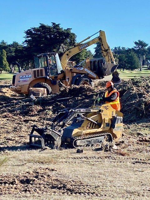 Construction site with Case backhoe and compact loader, worker in safety vest, outdoor, daytime.