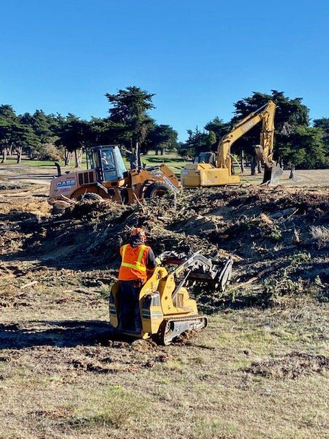 Construction site with heavy machinery and worker, possibly a golf course.