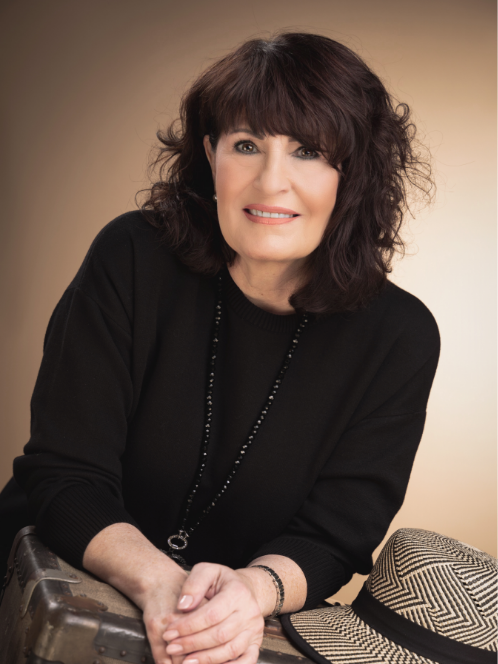 Eine Frau mit schwarzem Pullover und Hut sitzt mit gefalteten Händen da