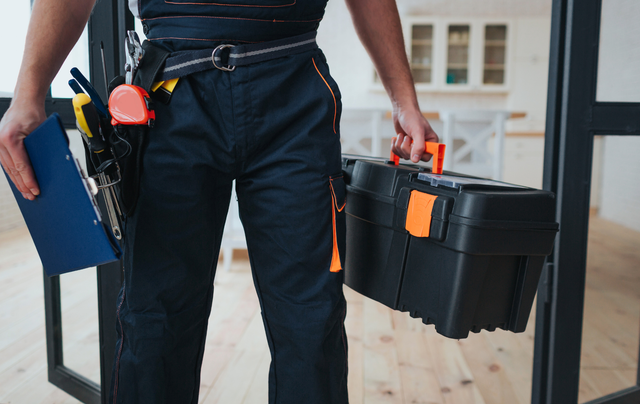 A man is holding a toolbox and a clipboard.